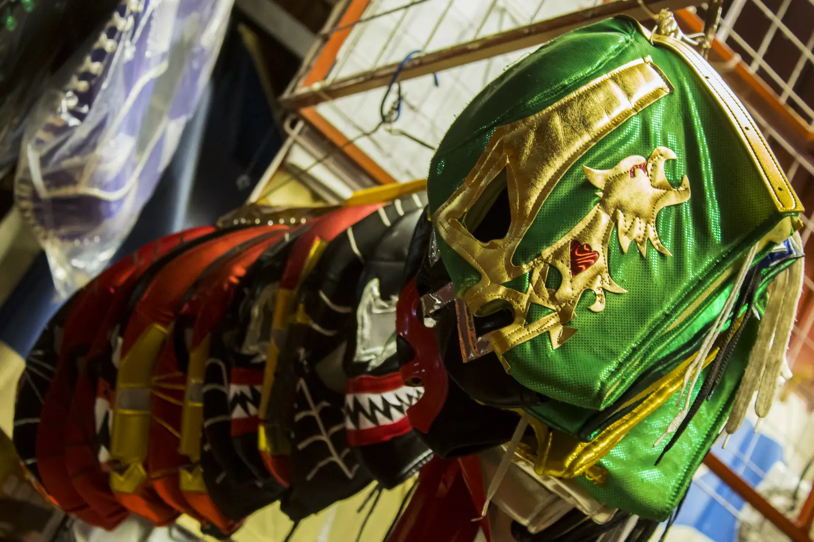 Rows of lucha libre masks hang on a market stall, with a green and gold mask in the foreground