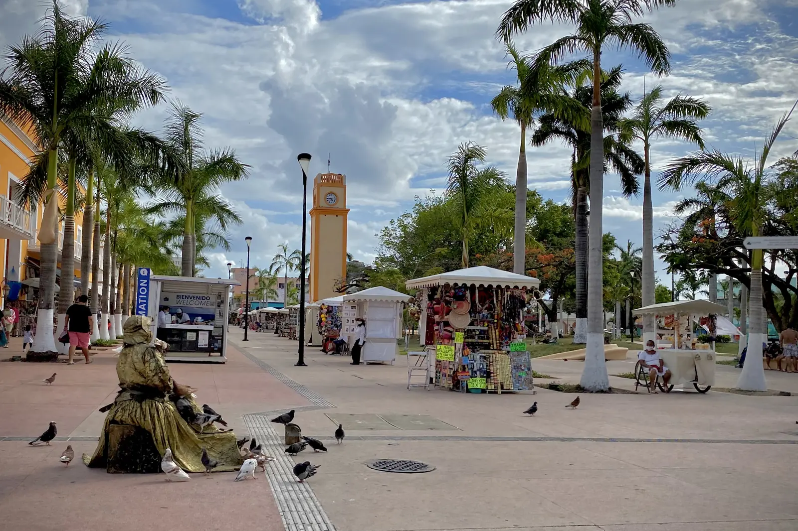 Palm trees, a clock tower and market stalls along a paved plaza in San Miguel de Cozumel